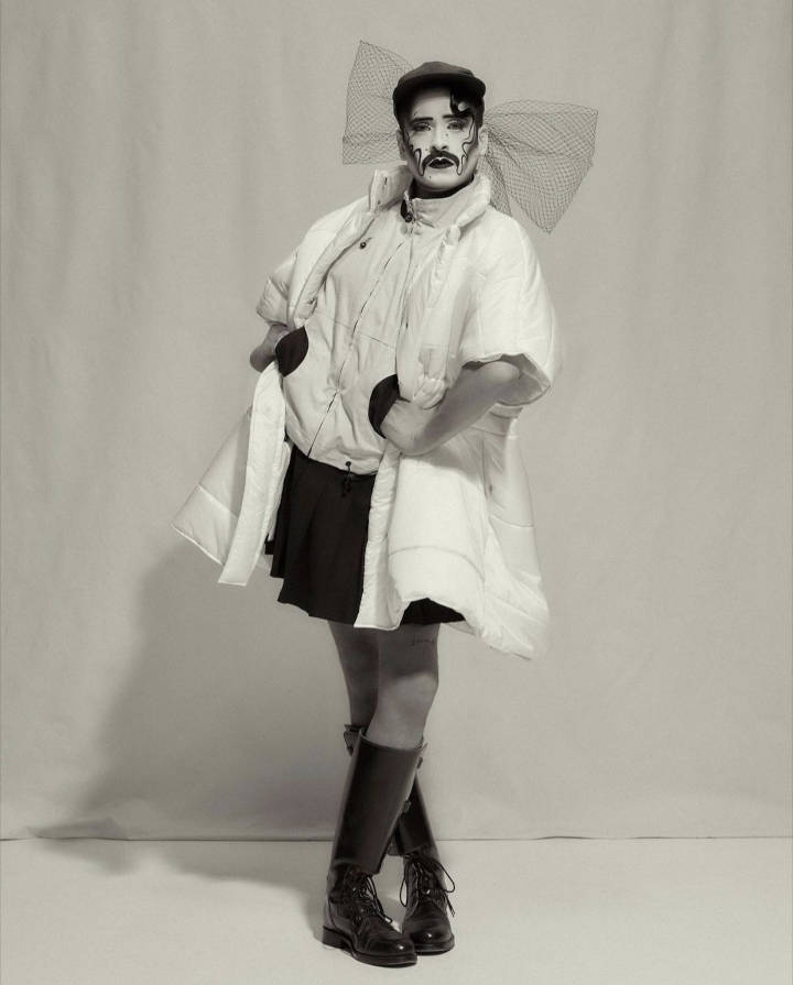 Continental Breakfast, posed with hands on hips, wearing a white puffer jacket, skirt, and hat with a large mesh bow