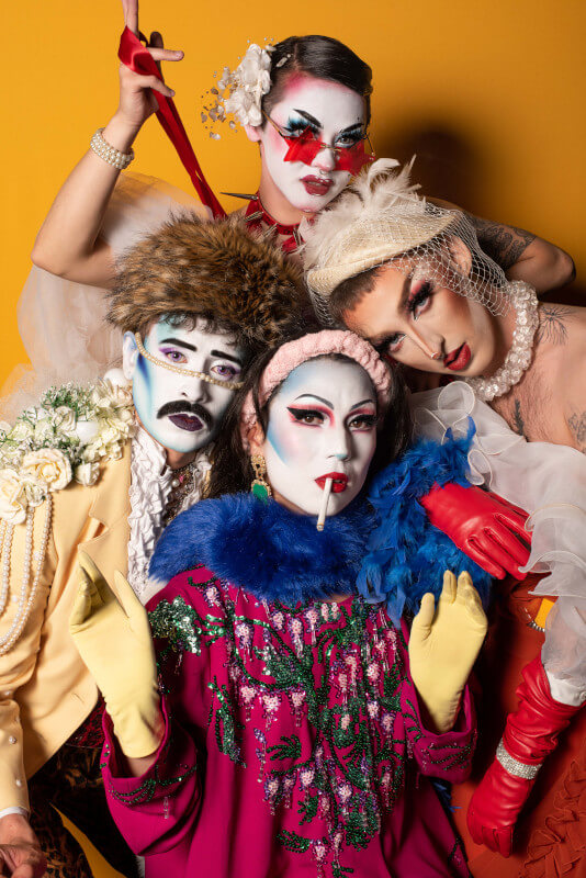 The Darlings in bright, multicolored clothes against a yellow backdrop