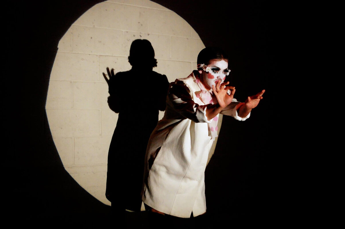 Rose performing in front of a brick wall with a spotlight trained on them.