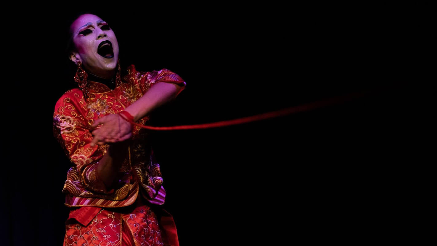 Maiden performing in a red gown, holding up their hands bound with red string.