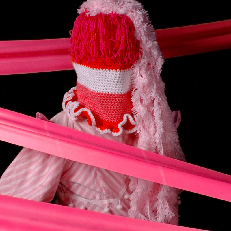 PM in a pink knit face covering, surrounded by pink ribbons.