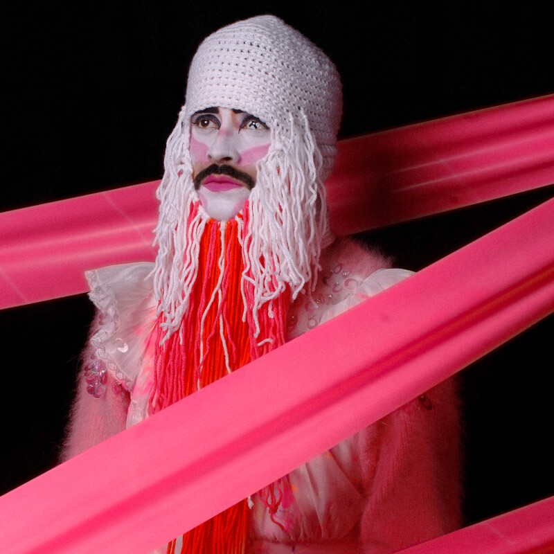 Conti in a white knit face covering, surrounded by pink ribbons.